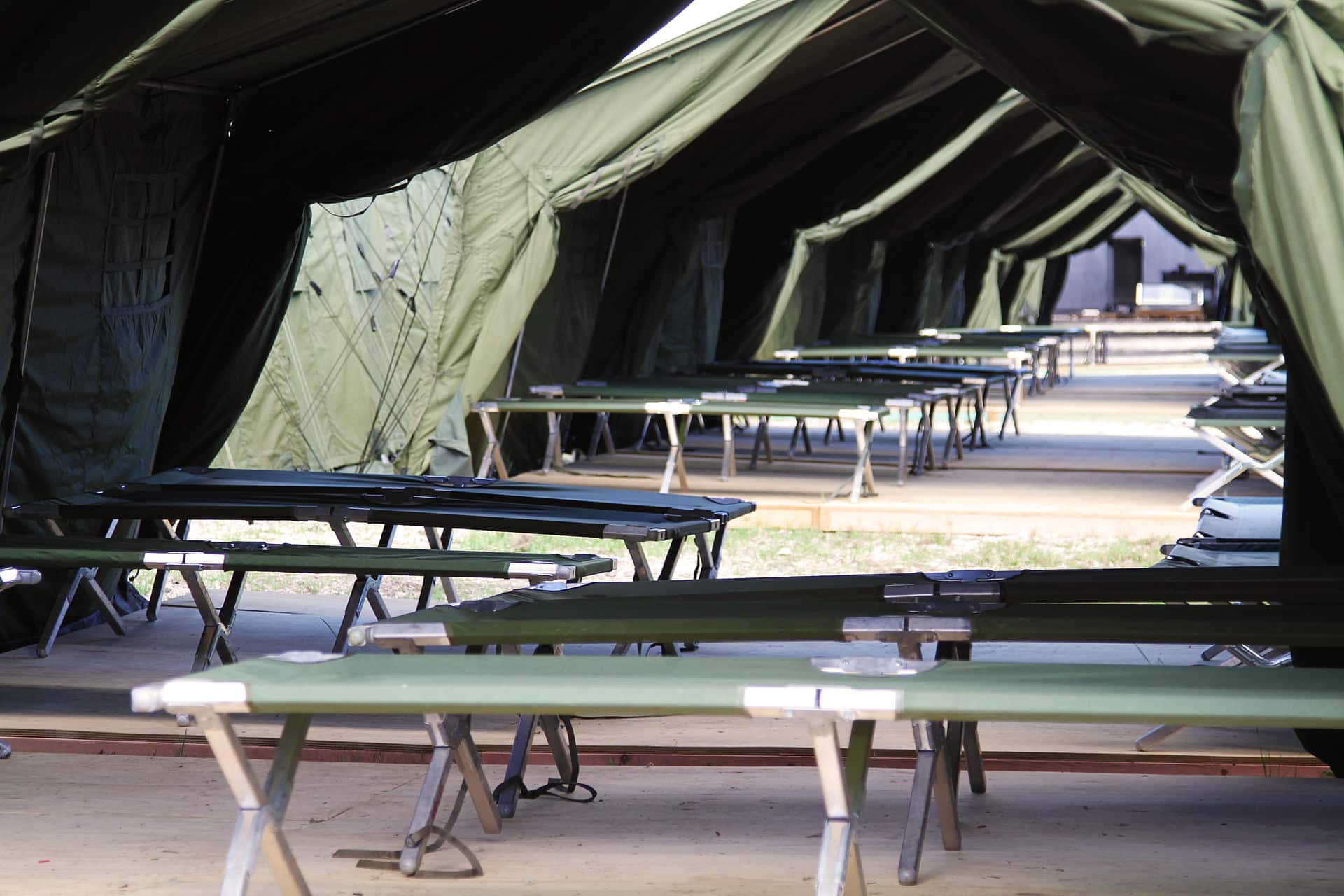 Green tent that is open on the sides. There are multiple benches on the ground underneath it.