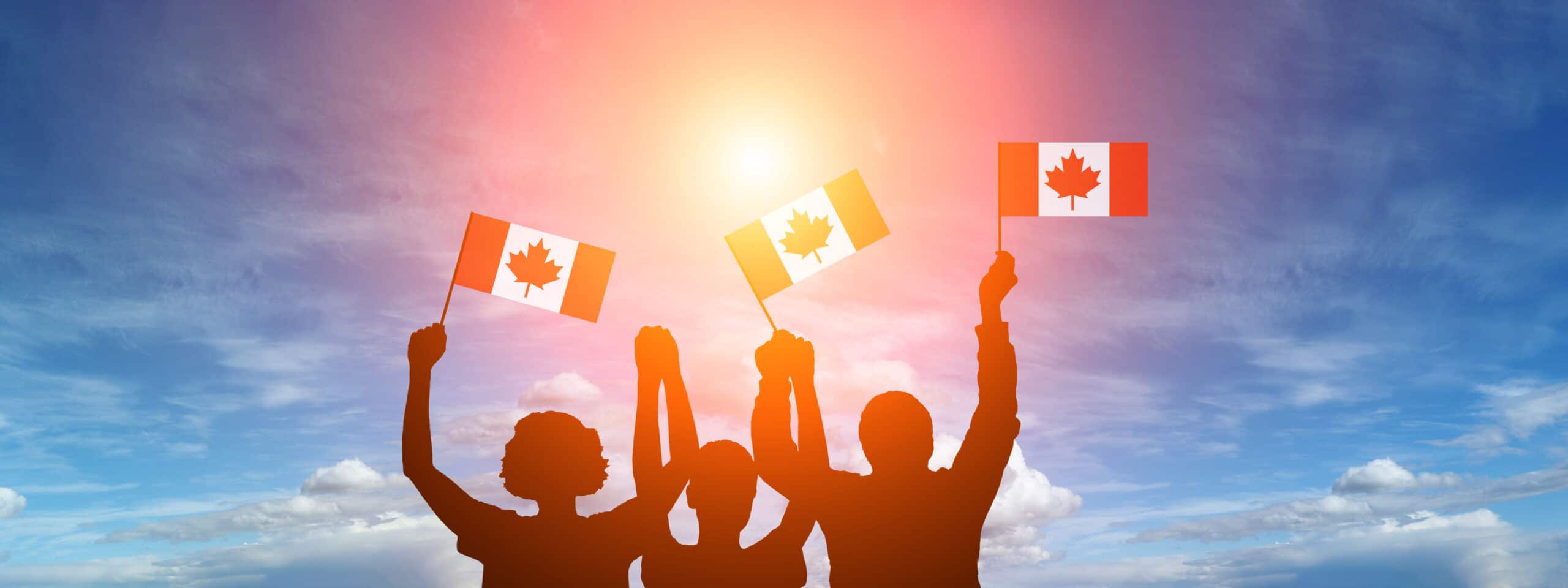 Three silhouetted figures waving Canadian flags. They are standing against a blue sky with clouds.
